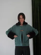 Campera corta color verde agua con cuello y puños de piel sintética marrón oscuro. Cierre frontal con broches tipo toggle de madera.