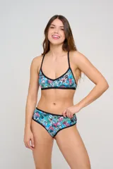 Corpiño de bikini estampado con diseño floral colorido en tonos fucsia, naranja y celeste, con ribetes negros y tirantes cruzados en la espalda.