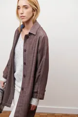 Spolverino largo de jean color azul, con cuello camisero, botones frontales y costuras decorativas en blanco.