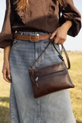 Bandolera de cuero negro, de diseño rectangular y compacto, con correa ajustable para llevar cruzada al hombro. Cuenta con un bolsillo frontal con cierre y detalles de costuras pespuntadas a contratono.