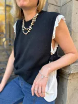 Chaleco tejido de punto en color negro, con cuello redondo a la base y diseño sin mangas. Presenta aberturas laterales con lazos ajustables que permiten regular el calce.