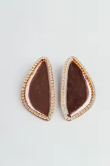 Par de aros colgantes con forma abstracta rellena de resina color marrón y bordes con strass dorados.