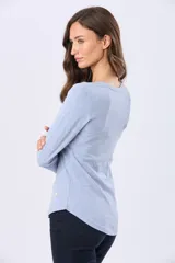 Remera de manga larga en color celeste melange, con cuello redondo y ruedo curvo. Presenta un pequeño aplique metálico decorativo en el lateral inferior.