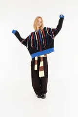 Sweater oversize de corte boxy, color negro con detalles en azul en cuello, puños y ruedo. Presenta flecos colgantes en colores rojo, amarillo y azul en la parte superior del frente y las mangas.