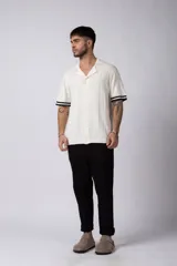 Camisa de punto de manga corta con cuello tipo bowling y cierre frontal de botones. Presenta un diseño texturizado con franjas verticales y detalles de contraste en blanco en los bordes de las mangas.