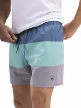 Short de baño de secado rápido, con cintura elástica y cordón ajustable. La parte superior es de color verde agua con un estampado de motivos circulares en tono azul oscuro. La parte inferior es de color terracota con un patrón de microperforaciones.