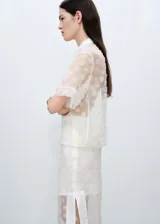 Camisa de manga corta con diseño recto y cuello camisero. Confeccionada en tejido semitransparente con bordado de flores pequeñas y cierre frontal con botones.