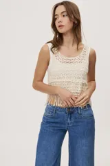 Top sin mangas de crochet color crudo, con escote redondo, diseño calado y terminación con flecos en el ruedo.