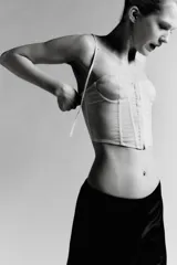 Corsé strapless color beige claro, con copas con aros y estructura de varillas verticales. El tejido es semitransparente con pequeños lunares visibles. Presenta un cierre frontal con ganchos.