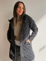 Campera larga de diseño capitoneado con patrón de rombos, color negro. Cuenta con cierre frontal, botones a presión, capucha y bolsillos laterales.