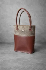 Cartera matera de cuero marrón con diseño bicolor, detalles de costuras visibles y aplique metálico en forma de caballo.