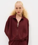 Campera de modal color marrón, con cuello alto, cierre frontal completo y diseño con pliegues en el ruedo. Presenta mangas largas y un calce holgado.