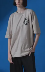 Remera de manga corta y cuello redondo con calce oversize, color beige con estampa gráfica en negro que incluye texto y un rostro femenino estilizado con llamas.