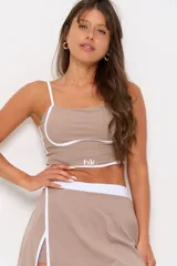 Conjunto deportivo compuesto por un top de tirantes finos con detalle de ribete blanco y logo estampado, y una pollera short con cintura elástica blanca y diseño cruzado con ribetes blancos.