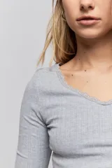 Remera de manga larga en tejido acanalado color gris, con escote en V y detalle de puntilla en el borde del cuello.