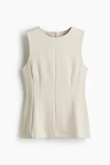 Top sin mangas de color beige confeccionado en punto roma, de corte entallado con costuras moldeadoras delanteras y traseras, cierre oculto en la espalda y detalle de peplum en la parte inferior.
