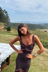 Vestido largo color chocolate, ajustado al cuerpo, con tirantes finos y escote en V. Presenta detalles de flecos en el escote y en la abertura lateral de la falda.