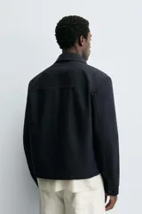 Cazadora cropped fit color azul marino, confeccionada en tejido de algodón. Presenta cuello solapa, manga larga con puño abotonado, bolsillos frontales de vivo y un bolsillo interior. El cierre es frontal con cremallera.