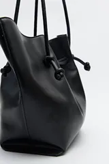Bolso tipo tote bag negro de cuero sintético, con frunce superior ajustable con cordones y doble asa de hombro.