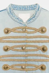 Chaqueta de mezclilla clara estilo militar, con cuello redondo, manga larga y detalles de cordones y botones dorados en el frente.