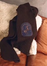 Bufanda tejida a mano de color marrón oscuro, con un parche bordado que incluye la ilustración de un caballo y la inscripción 'The Ranch Dress Code'.