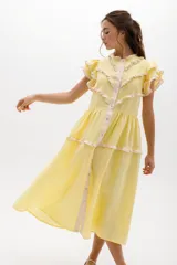 Vestido midi de lino blanco con diseño de broderie, cuello alto, cierre frontal con botones y volados decorativos en los hombros y el cuerpo.