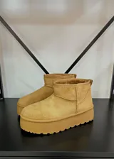 Botas cortas de gamuza color tostado con plataforma plana y suela dentada. Presentan un diseño minimalista con costuras reforzadas y forro interior de peluche.