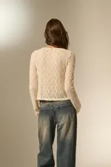 Top de encaje color natural, de manga larga y diseño holgado, con cierre frontal mediante lazos anudables y cuello redondo.