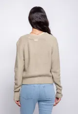 Cardigan color beige con trama de punto trenzado, cuello en V y cierre frontal con botones.