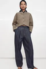 Chaqueta corta de corte estructurado confeccionada en tejido con mezcla de lana. Presenta cuello en pico, cierre frontal con botones y mangas largas. El diseño incluye bolsillos delanteros y un forro interior a contraste.
