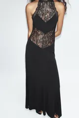 Vestido largo negro de cuello halter con detalles de encaje en la parte superior y espalda. Cuenta con corte en línea evasé y cierre posterior con abertura y botón.