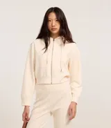 Saco color crema, de corte slim, confeccionado en algodón con viscosa certificada, con cuello con capucha y cordón ajustable, cierre frontal con cremallera y forro de fleece.