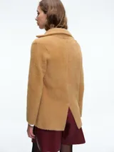Saco corto de tejido de punto con textura suave, diseño estructurado con hombreras, solapas clásicas y bolsillos frontales. Posee cierre frontal y un corte que define la silueta.
