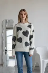 Sweater de punto en color beige con estampado de corazones negros, cuello redondo y mangas largas con puños acanalados.