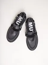 Mocasines de cuero negro con plataforma, diseño tipo náutico con costuras reforzadas en la puntera, detalle de tira sobre el empeine con apliques metálicos y argollas laterales.