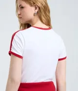 Remera blanca de algodón con estampa frontal de Mickey Mouse y detalles en color rojo en cuello y mangas. Presenta un diseño ajustado con líneas laterales en las mangas.