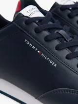 Zapatillas Tommy Hilfiger azul marino de corte bajo, con logo en el lateral y detalle rojo en el talón. Suela blanca dentada de goma.
