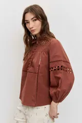 Camisa de manga larga abullonada color marrón, con detalles de bordados calados en el pecho y las mangas, y cierre frontal con botones.