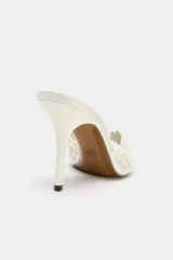 Sandalia de tacón alto estilo mule, de color blanco crudo, con diseño en la pala en forma de concha decorada con perlas y cuentas brillantes, punta cuadrada y tacón fino.