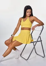 Conjunto deportivo compuesto por un top con cuello halter y una pollera short con diseño plisado, ambos en color amarillo.