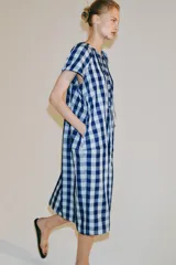 Vestido midi de Zara Woman Collection confeccionado en mezcla de viscosa, con estampado de cuadros en tonos azul y celeste. Presenta cuello redondo, manga corta, bolsillos ocultos en las costuras y cierre frontal con cordones entrelazados.
