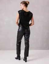 Blusa de lentejuelas color negro, con cuello a la base, sin mangas y detalle de nudo en el ruedo.