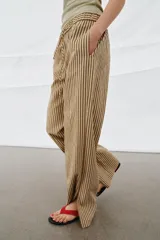 Pantalón de tiro medio con diseño de rayas verticales en tonos beige y marrón. Presenta una cintura elástica ajustable con cordones, bolsillos laterales ocultos y corte de pierna recta con aberturas en el bajo.