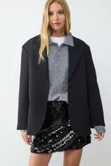 Blazer negro de corte recto y diseño oversize, con cuello de solapa, cierre frontal de dos botones y bolsillos con solapa en los laterales. Interior forrado.