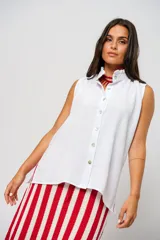 Camisa blanca sin mangas con cuello mao adornado con un delicado volado y cierre frontal con botones.