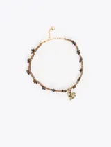 Gargantilla de cordón trenzado color tostado con pequeñas piedras oscuras incrustadas, cadena de extensión dorada y dije colgante en forma de corazón con la inscripción "ti amo".