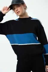 Buzo de punto con diseño de franjas horizontales en azul y blanco sobre fondo negro. Presenta cuello redondo, mangas caídas con puños elastizados y un corte holgado.