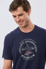 Remera azul marino de manga corta con cuello redondo, confeccionada en mezcla de algodón y poliéster. Presenta un estampado frontal circular de inspiración vintage con diseño de velero y tipografía alusiva a clubes deportivos.