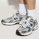 Championes urbanos New Balance modelo 530, con diseño retro de malla blanca y superposiciones en color plata y detalles en azul. Cuenta con entresuela con tecnología ABZORB para mayor amortiguación.