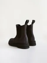 Bota tipo Chelsea de caña media, confeccionada en cuero negro con acabado mate. Presenta paneles elásticos laterales, tiradores traseros y suela track robusta con plataforma dentada.